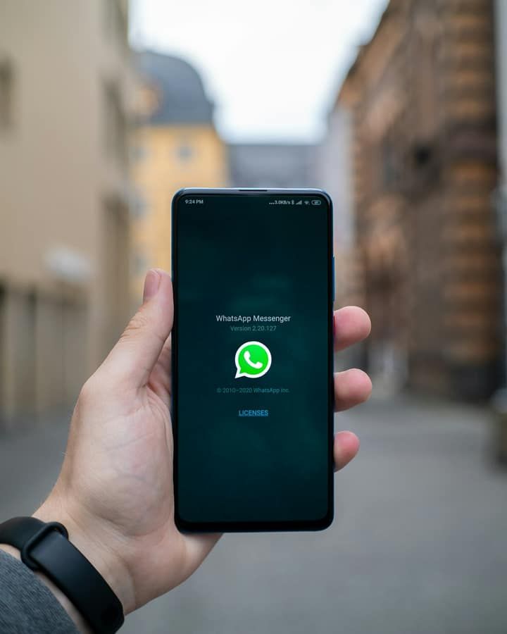 Tangan memegang ponsel Android yang menampilkan logo WhatsApp di jalan kota